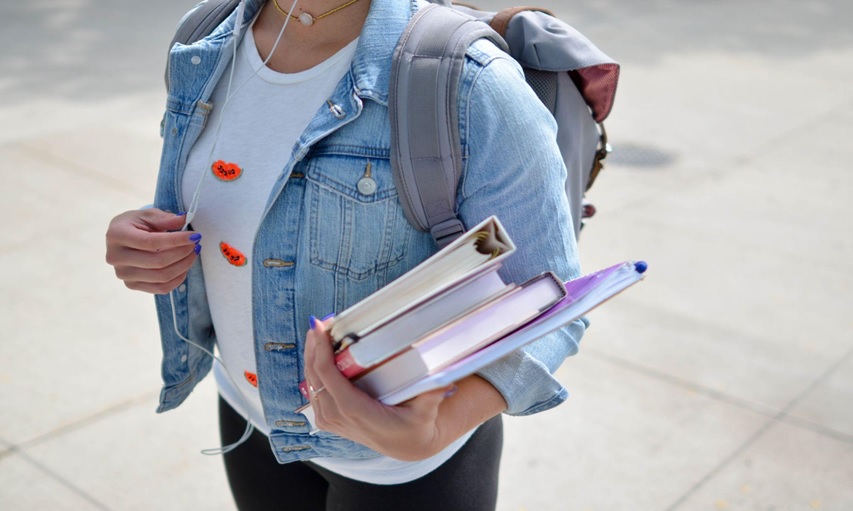 A student on their way to class, holding their books, and listening to music.
